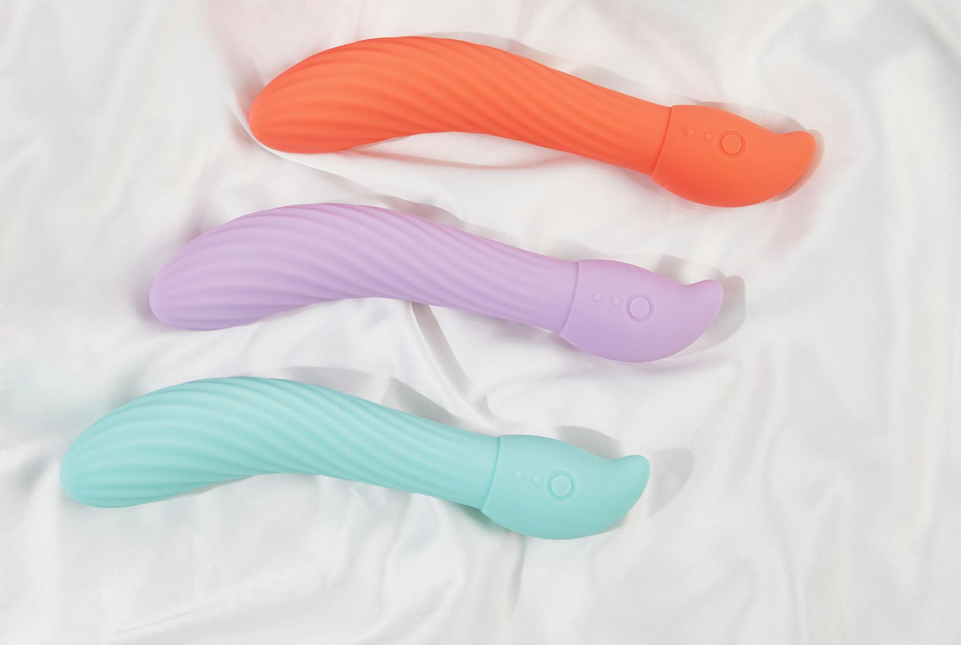 Colorful vibrators arranged on white fabric, highlighting their smooth texture.