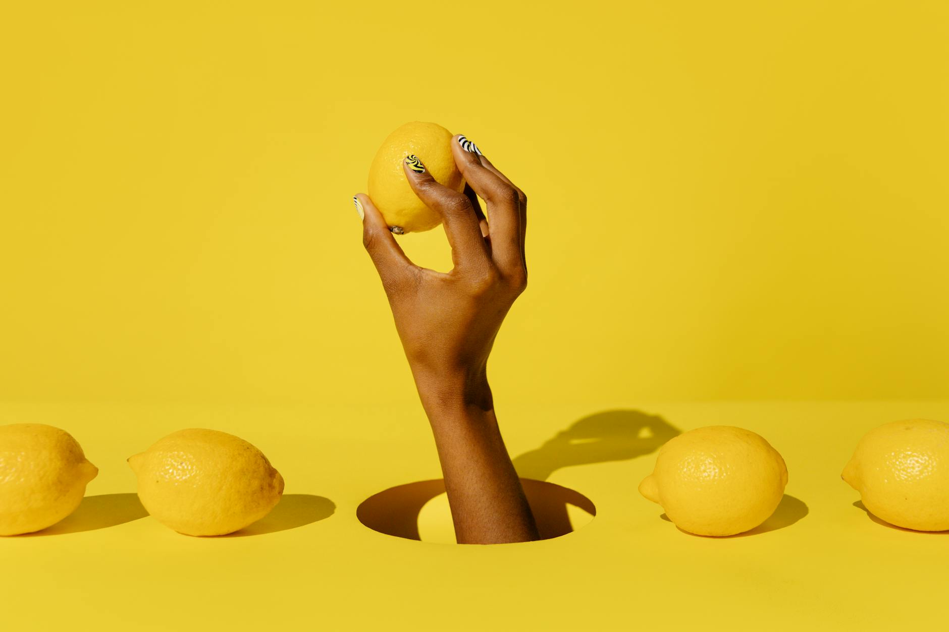 Hand holding a fresh lemon against a bright yellow background, symbolizing freshness and natural pleasure