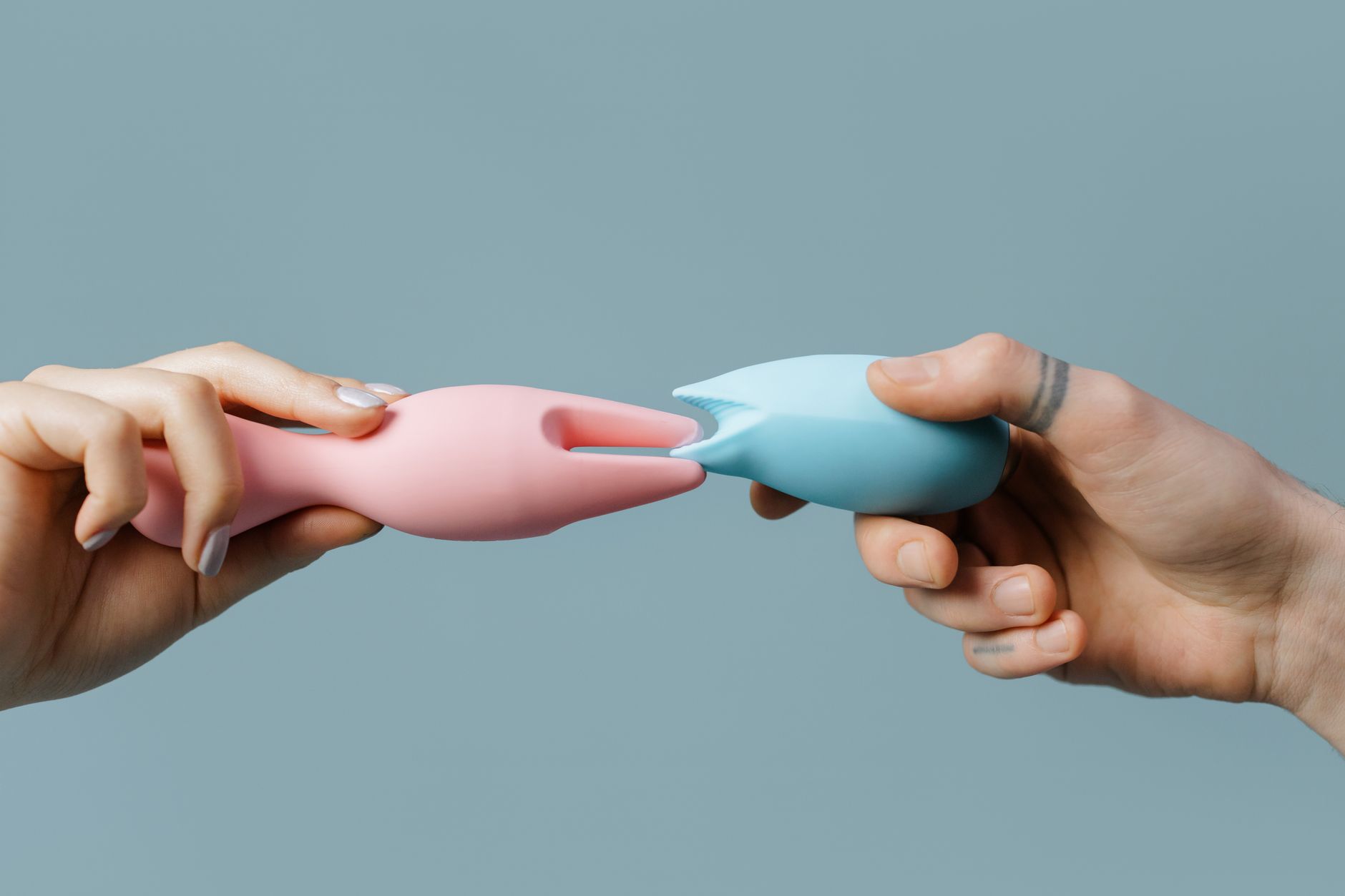 Hands holding pastel-colored silicone toys, representing clitoral vibrators and adult wellness