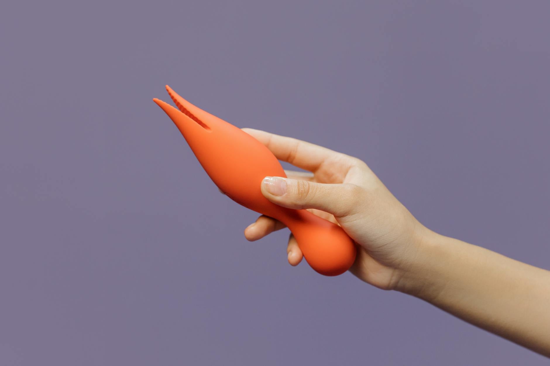 A hand holding a lemon-colored clitoral vibrator against a soft purple background